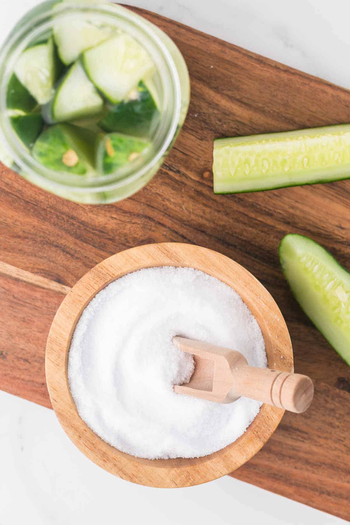 top view of a wooden bowl and spoon filled with pickling salt and sliced cucumbers