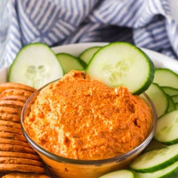 small dish with romesco sauce with crackers and chips and cucumbers around