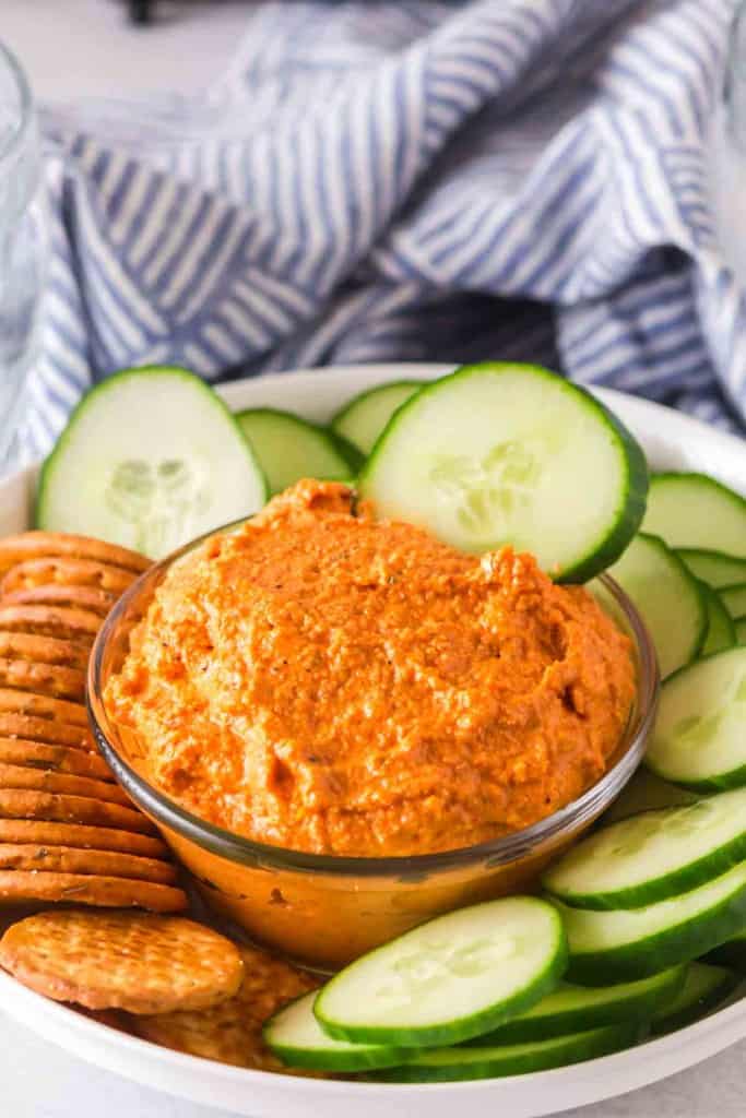 small dish with romesco sauce with crackers and chips and cucumbers around