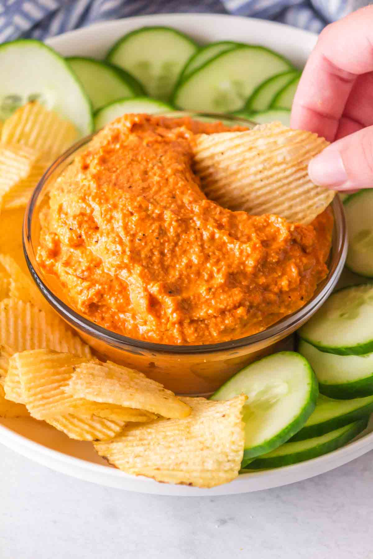 small dish with romesco sauce with crackers and chips and cucumbers around