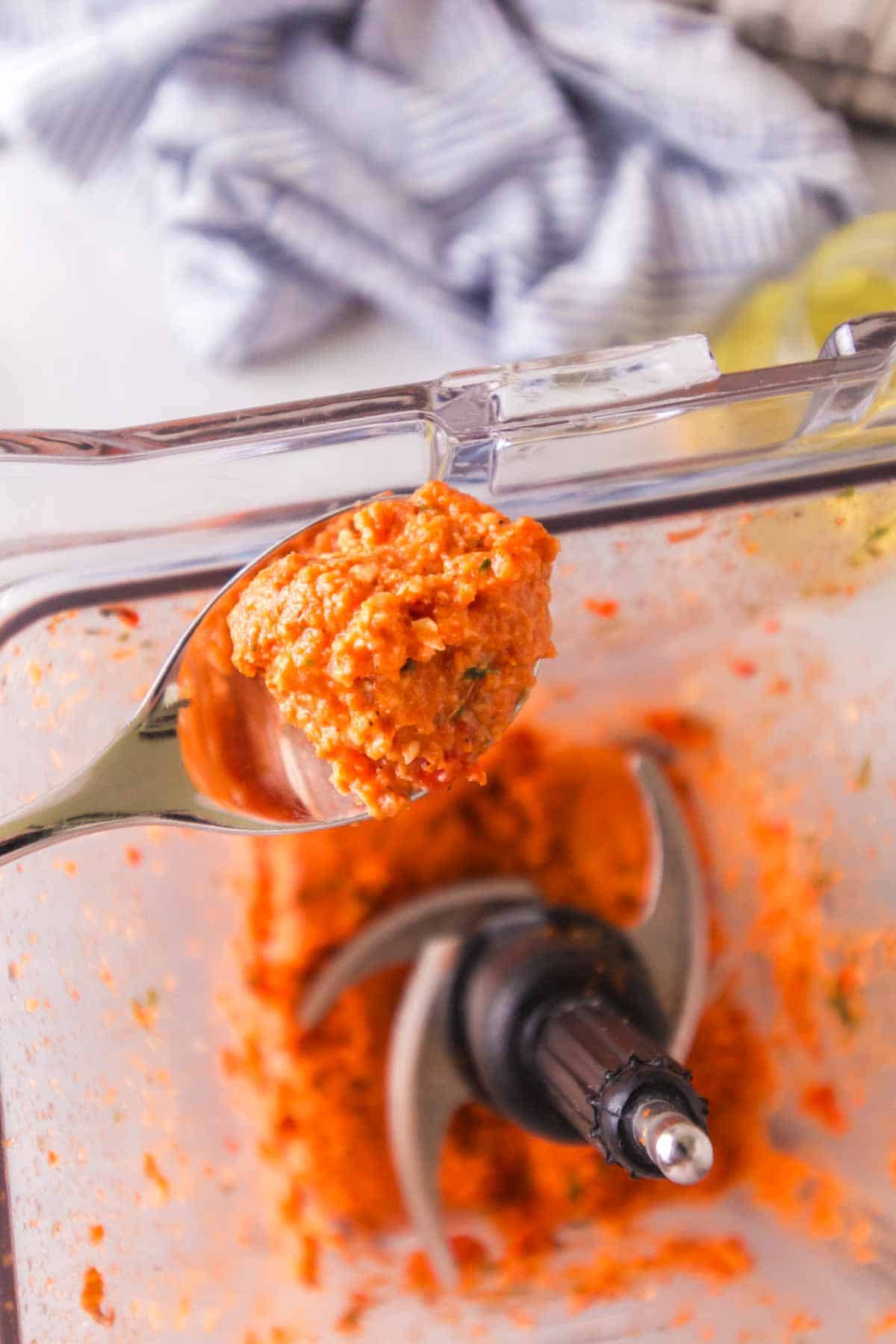 POV spoonful over a top view of a blender for romesco sauce
