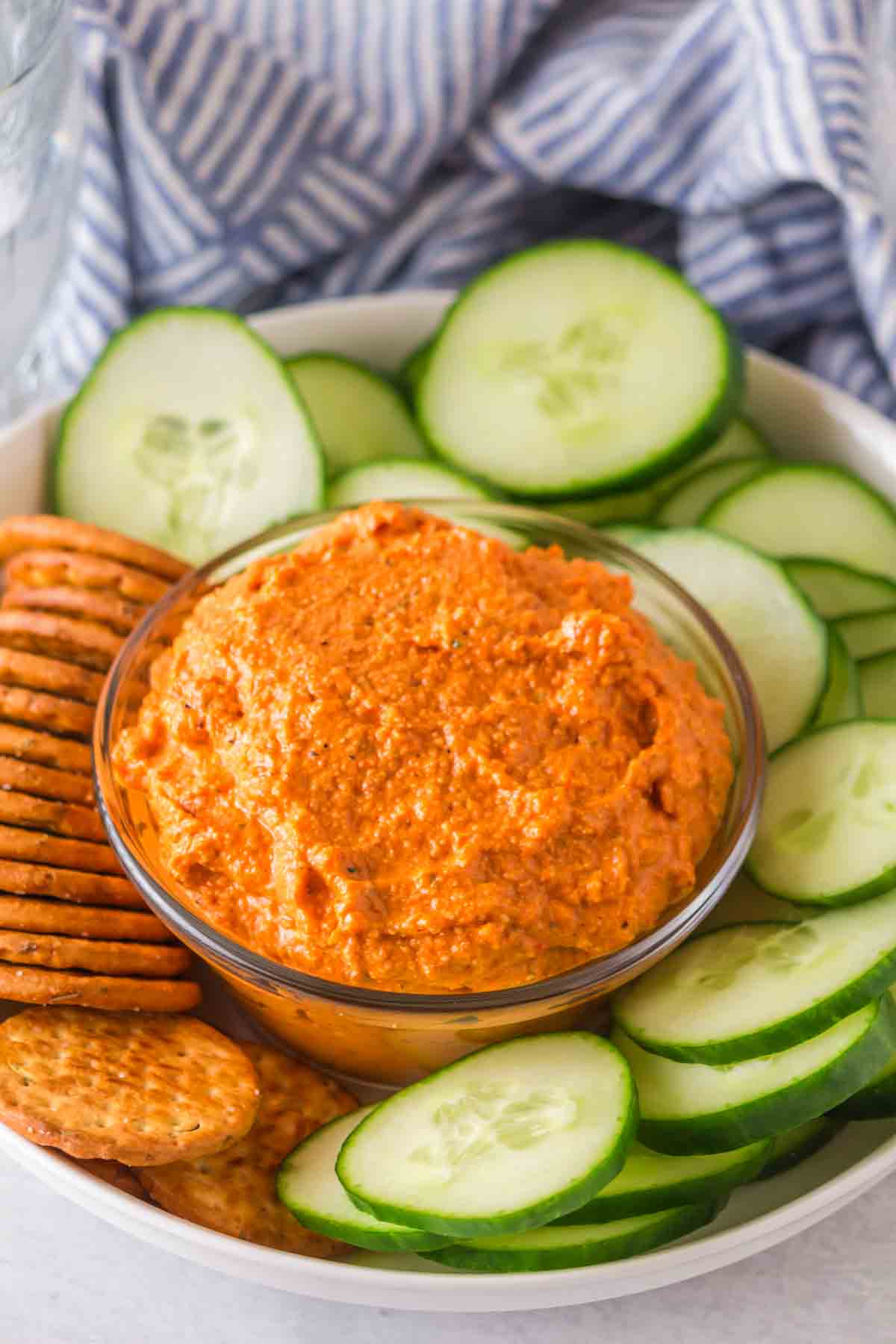 small dish with romesco sauce with crackers and chips and cucumbers around