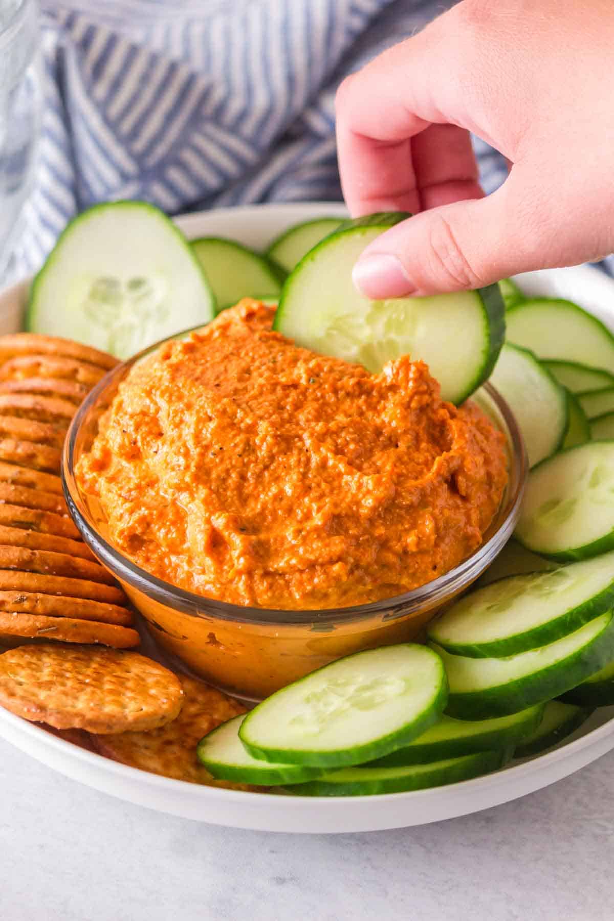 small dish with romesco sauce with crackers and chips and cucumbers around