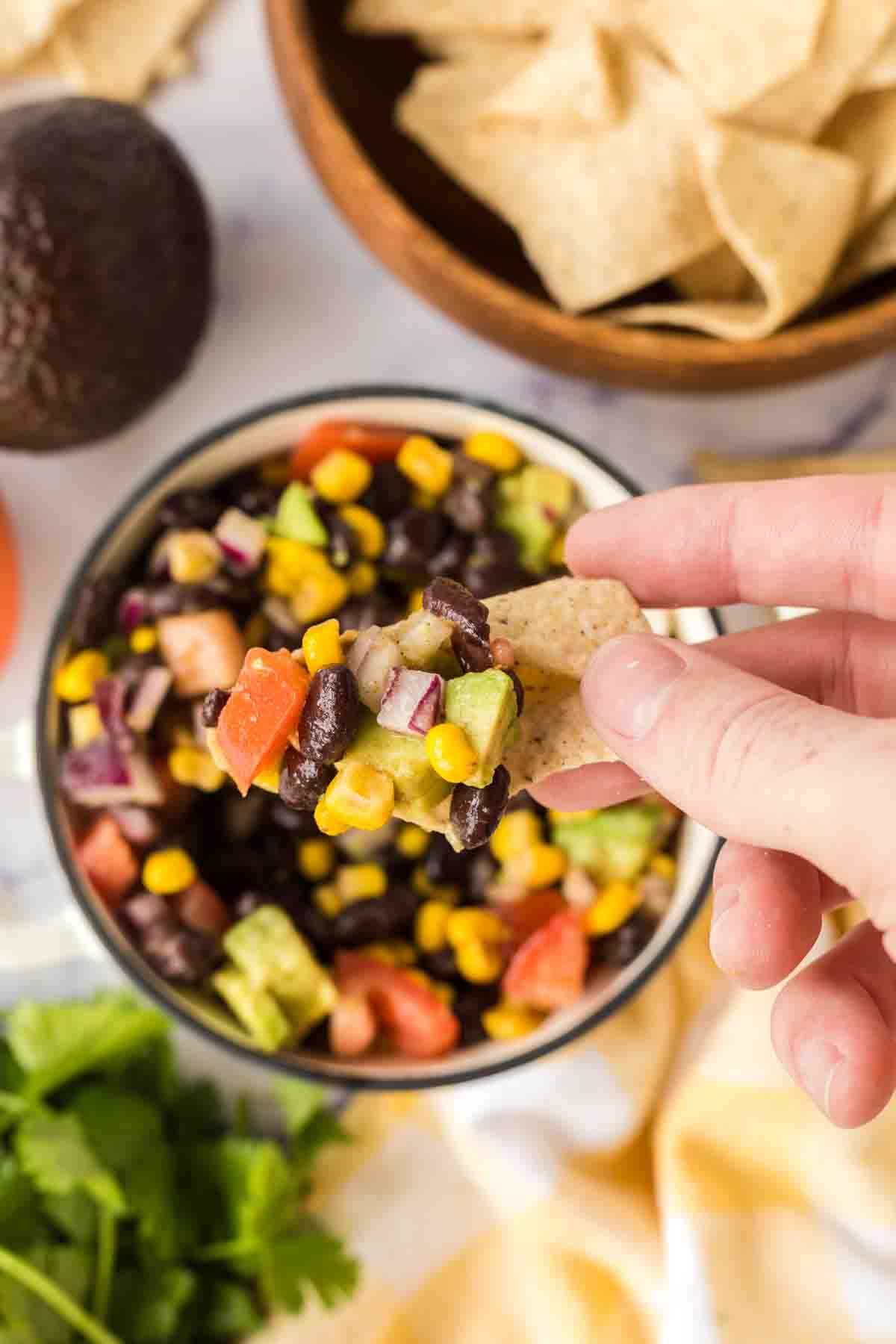 top view of a white dish of texas caviar recipe POV with a chip dipping in