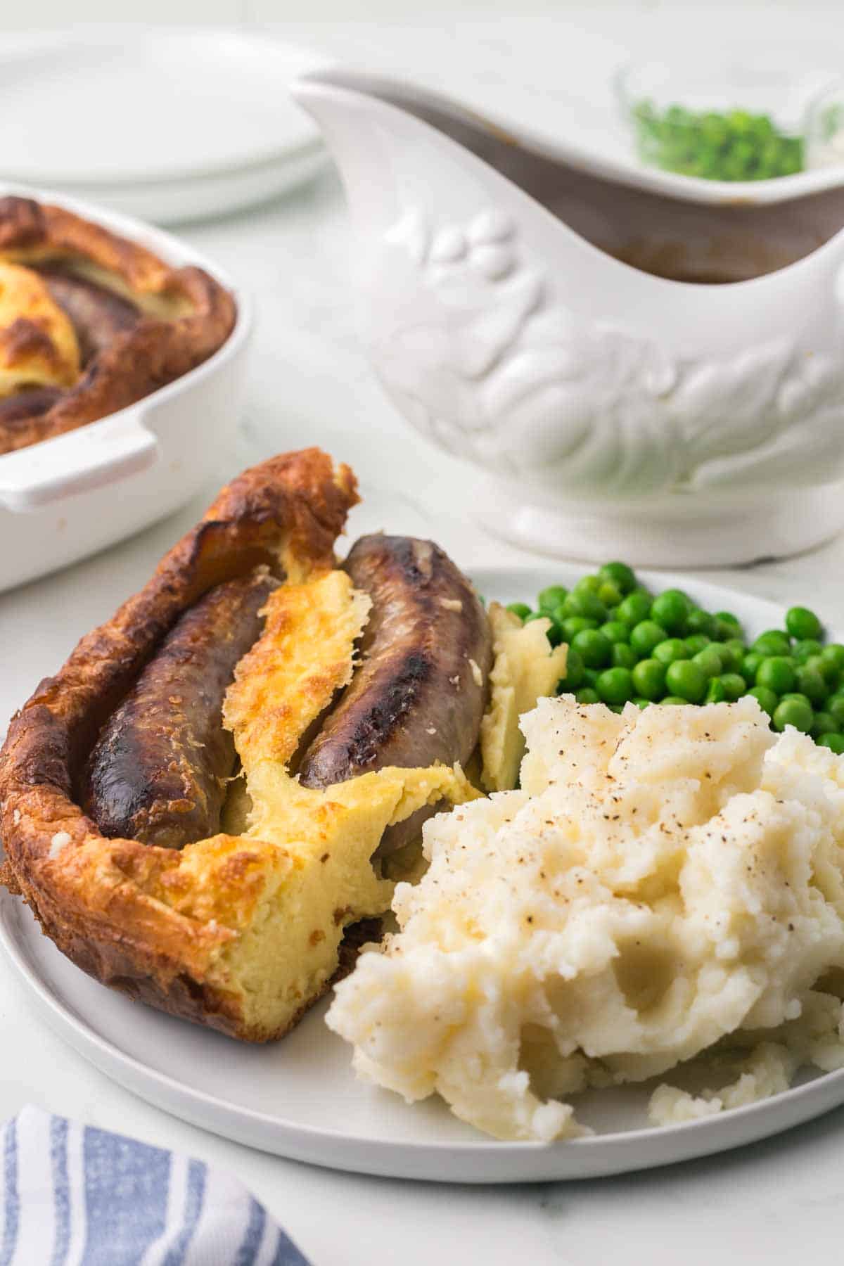 plated serving of toad in a hole recipe with mash potato and peas