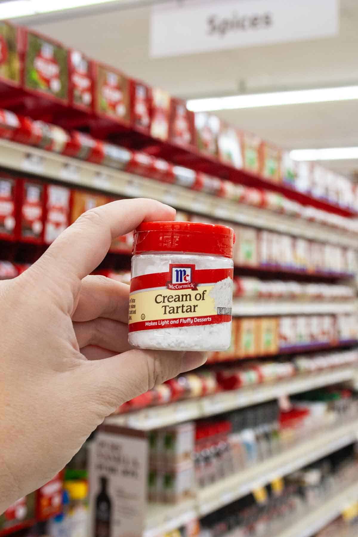 POV hand holding a small jar of McCormick cream of tartar with a red lid