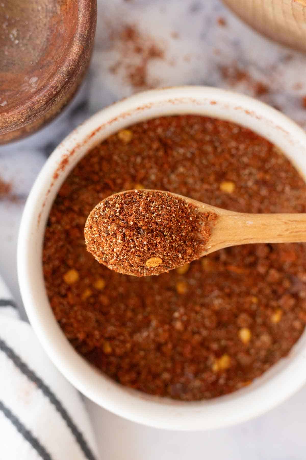 top view of a small white dish of adobo seasoning and a small wooden spoon