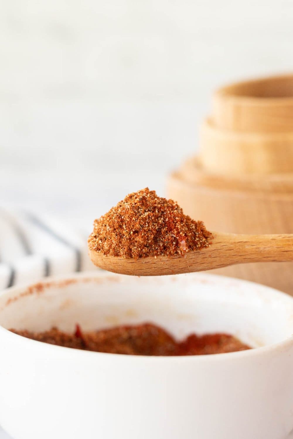 side view of a small wooden spoon over white dish of adobo seasoning