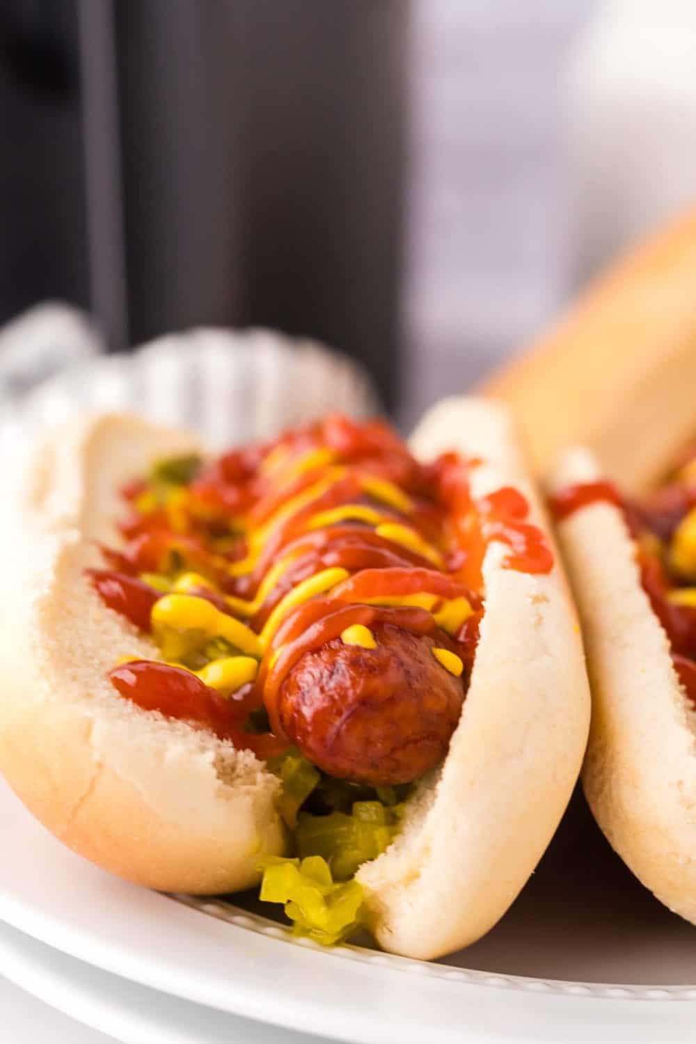 close up of the but end of two brats with ketchup mustard and relish in a traditional bun on a plate