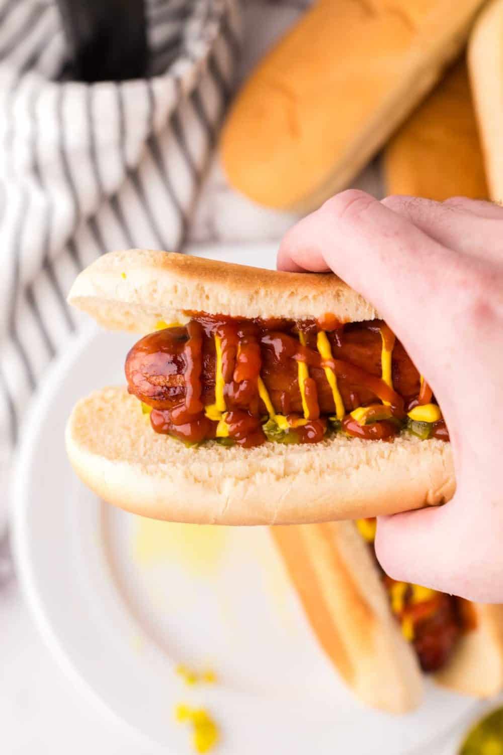 POV hand holding a brats with ketchup mustard and relish in a traditional bun