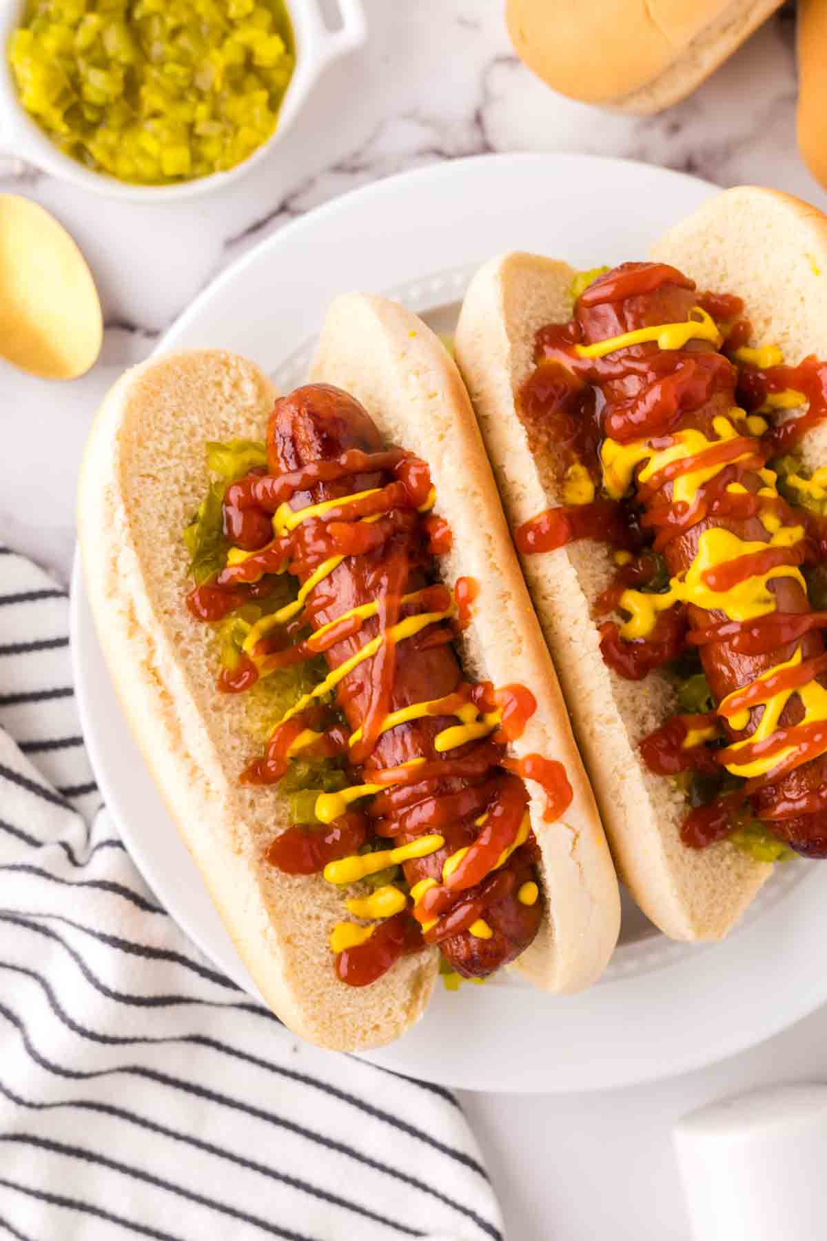 two brats with ketchup mustard and relish in a traditional bun