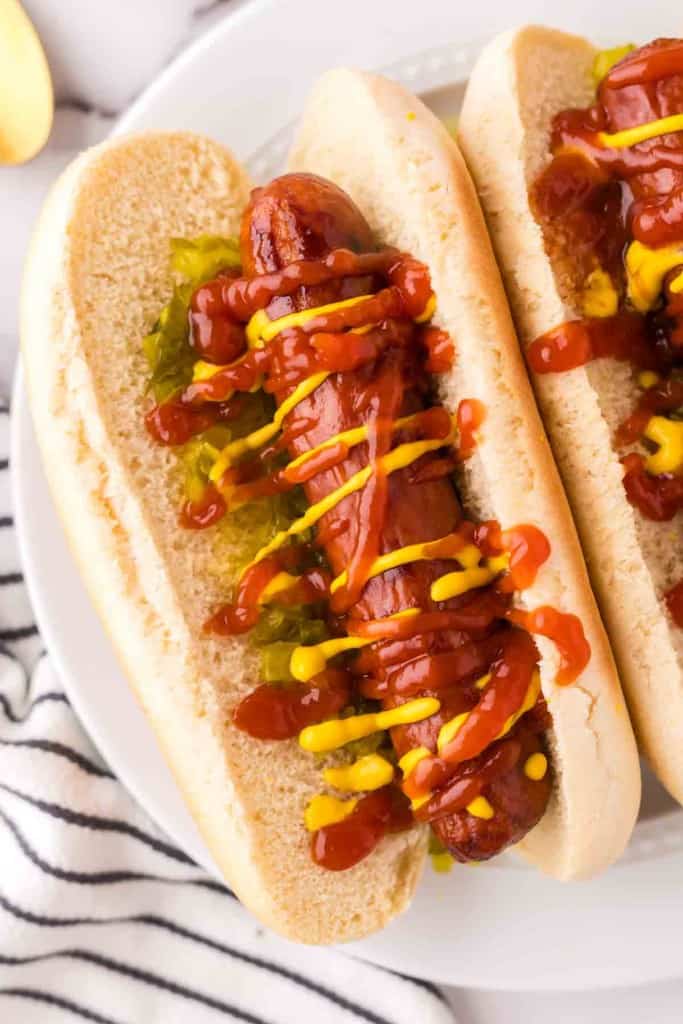 close up brats with ketchup mustard and relish in a traditional bun