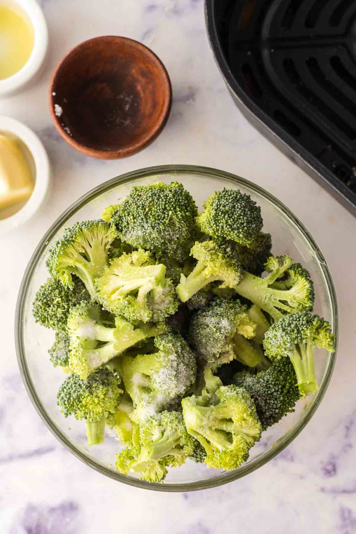 clear mixing bowl with broccoli being seasoned