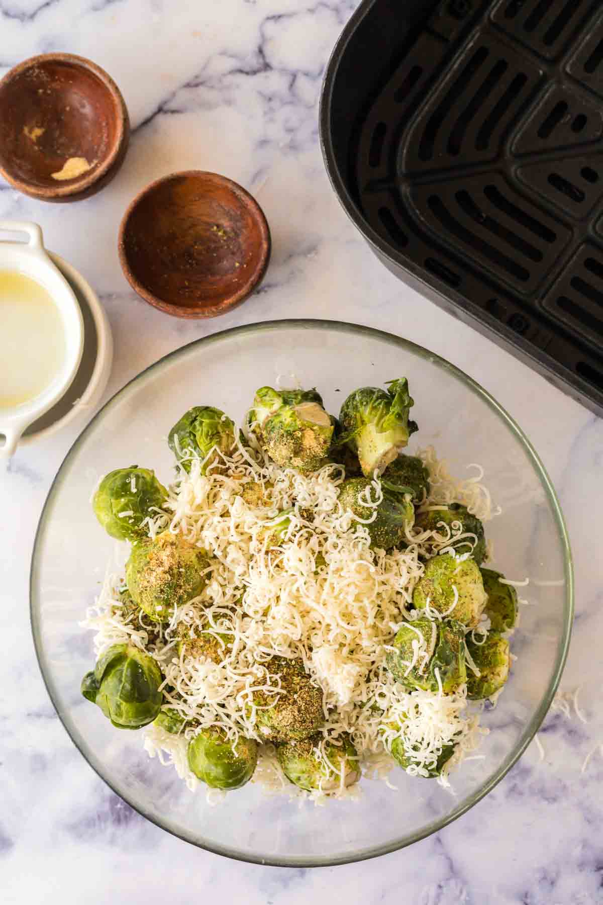 clear mixing bowl with cheesy and seasoned raw brussel sprouts
