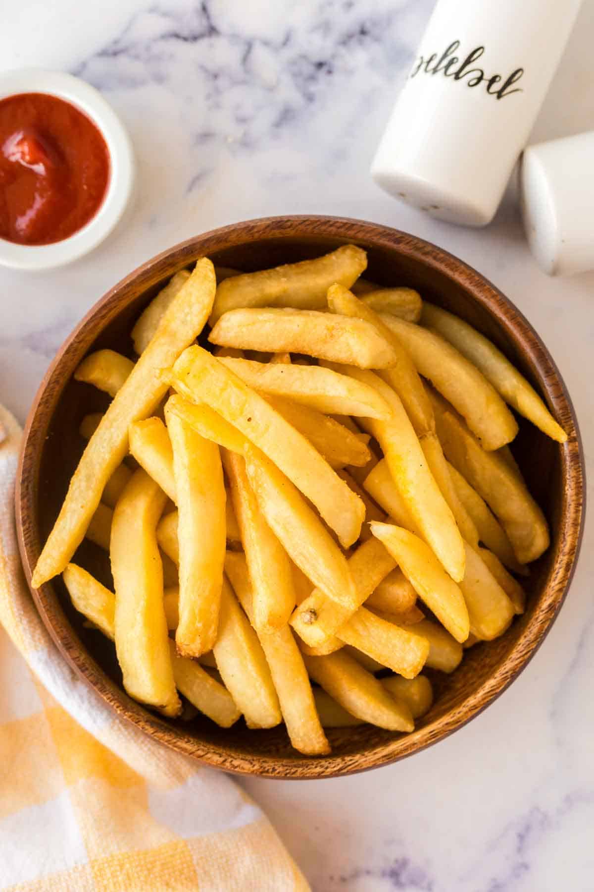 air fryer frozen french fries in a round wooden bowl with a dish of ketchup.
