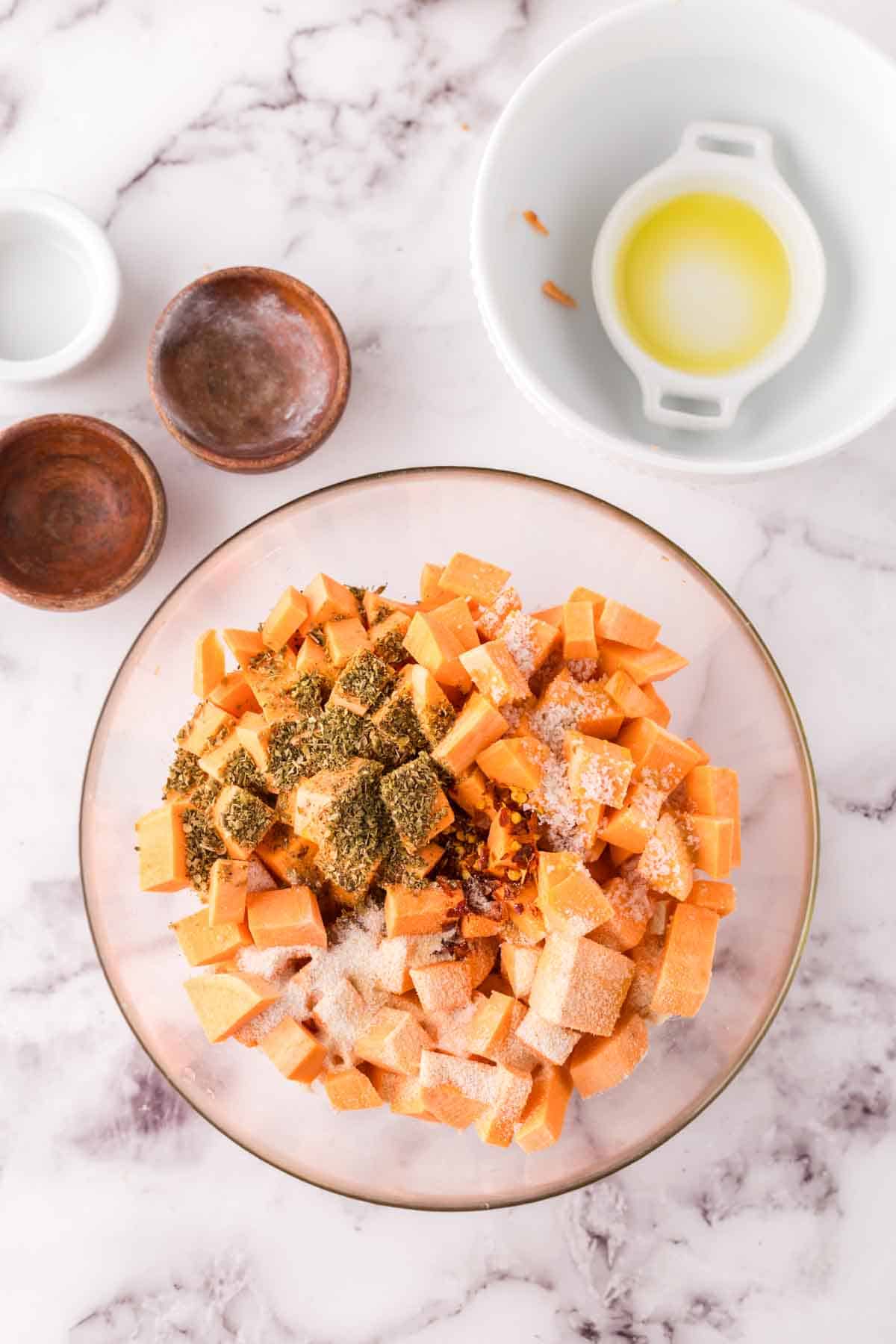 clear mixing bowl with seasoned raw sweet potato cubes