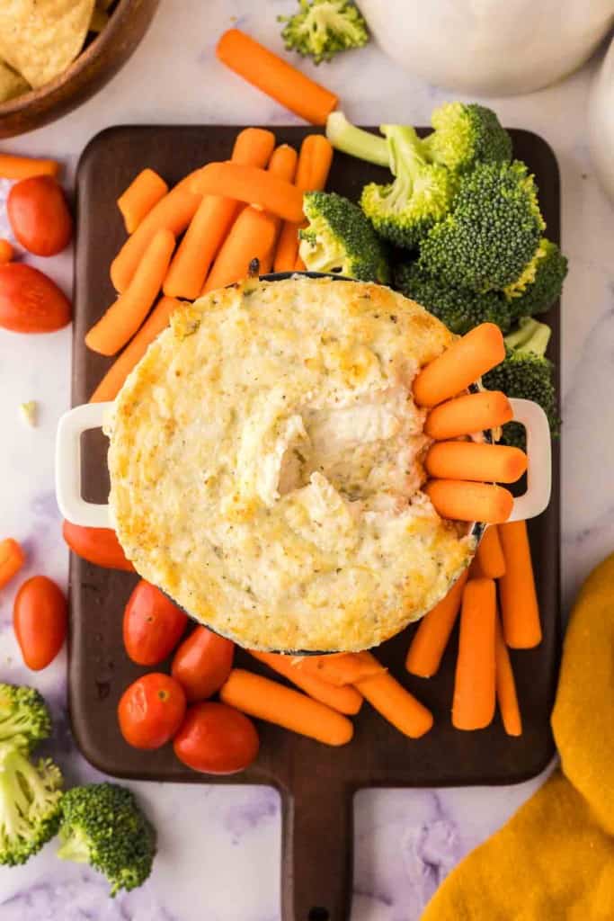 top view of carrots in a small bowl of artichoke dip recipe surrounded by other dip vegetables