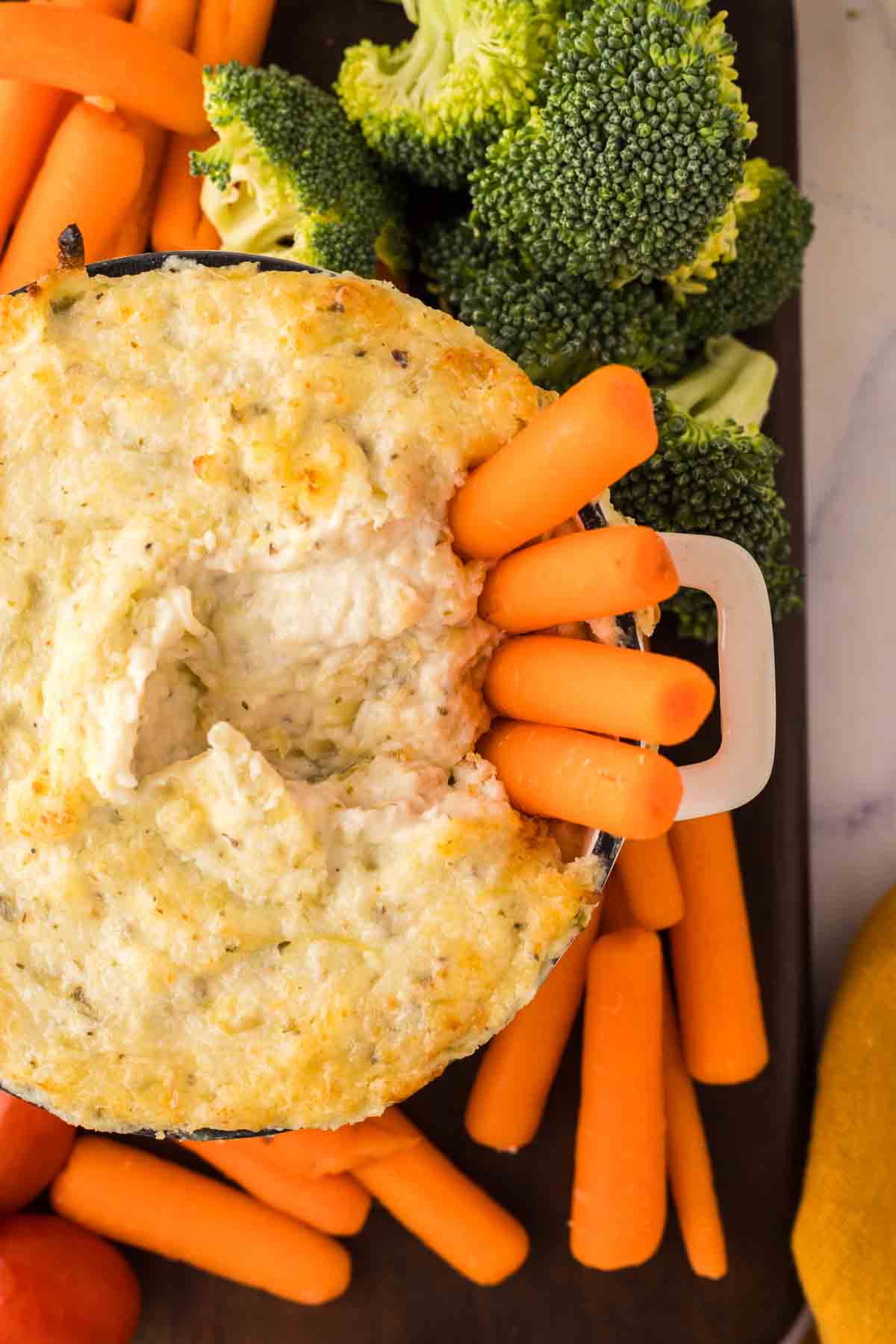 top view of carrots in a small bowl of artichoke dip recipe surrounded by other dip vegetables