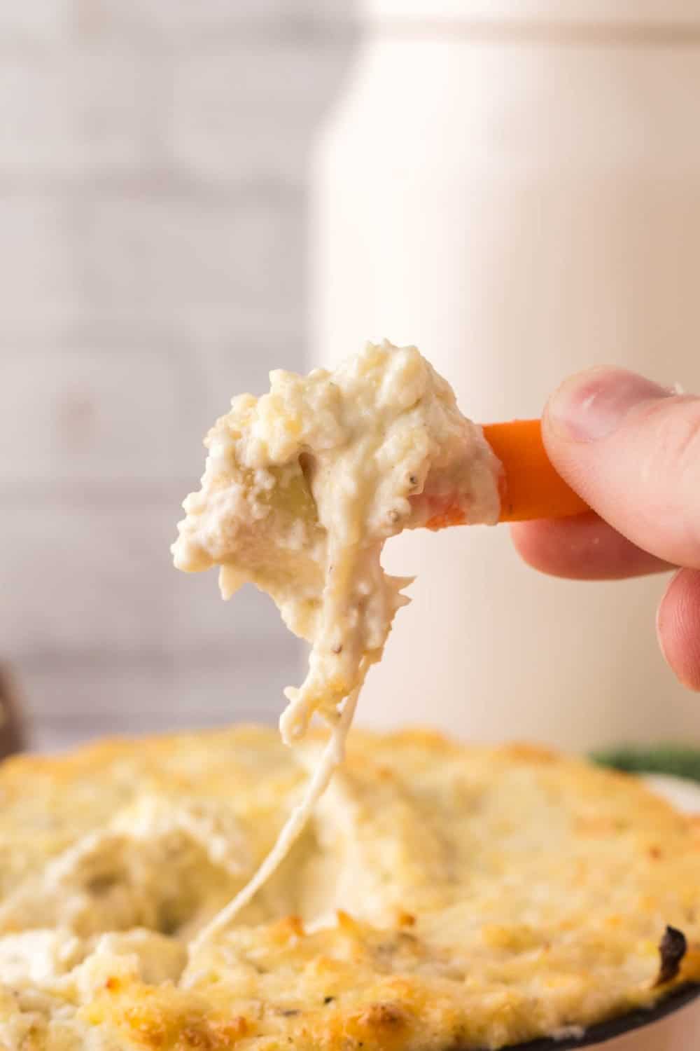 side view POV hand scooping a carrot in a small bowl of artichoke dip