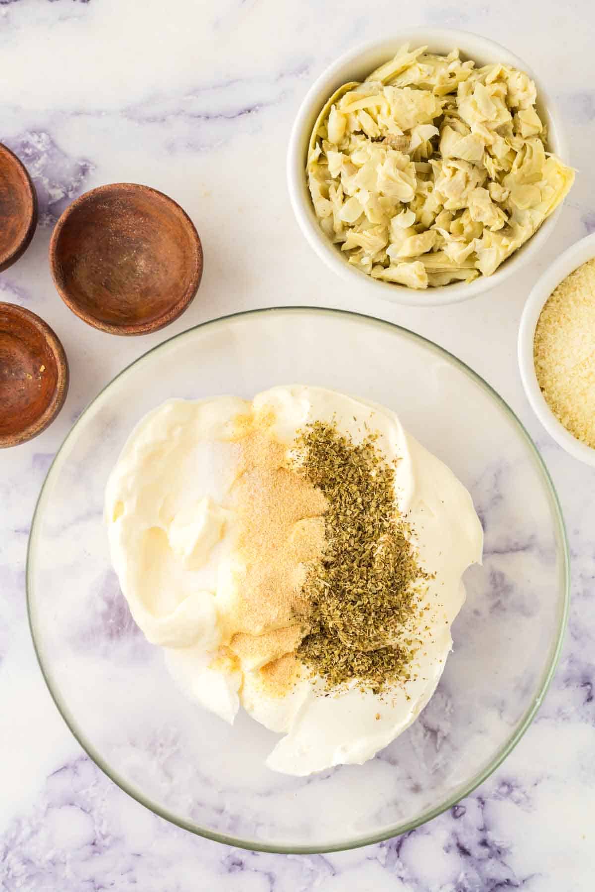 clear mixing bowl of the ingredients for artichoke dip recipe