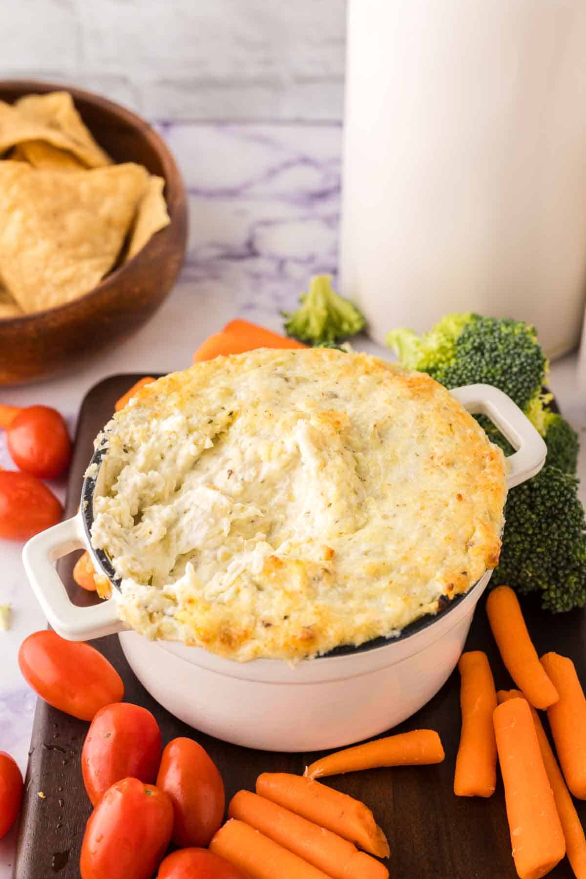 a bowl of baked artichoke dip on a tray of dipable veggies