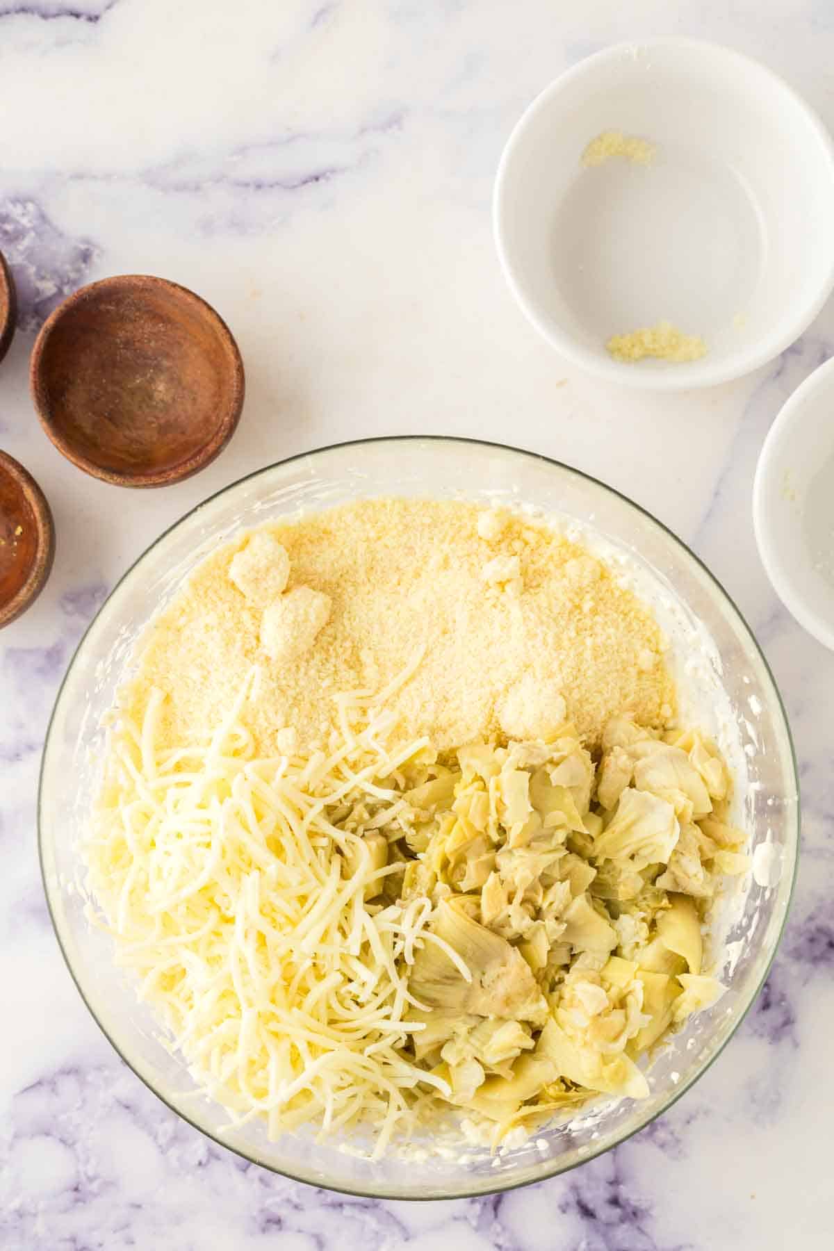 clear mixing bowl of the ingredients for artichoke dip recipe