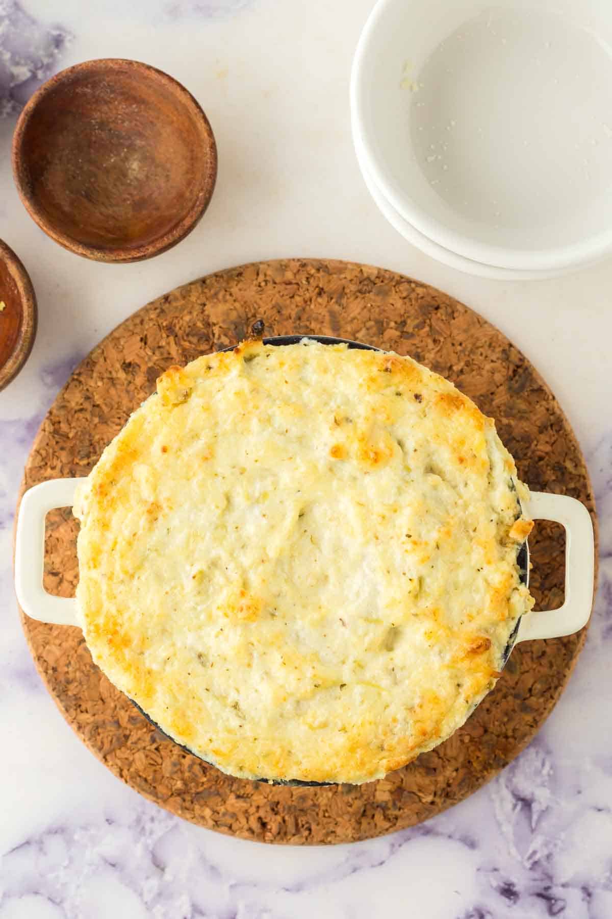 top view of a white bowl with golden baked cheese on top after the artichoke dip was baked and ready to eat