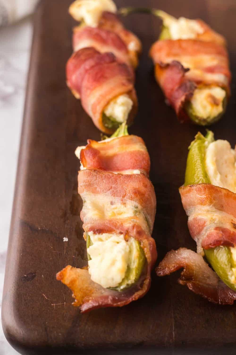 close up of bacon wrapped jalapeno poppers on a wooden board