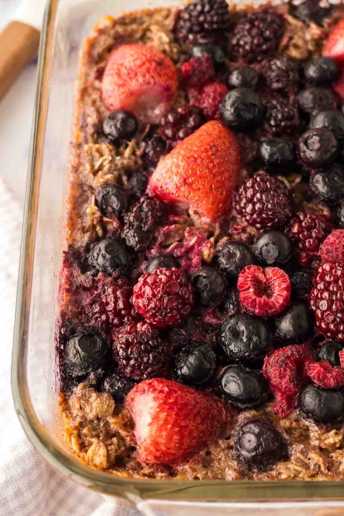 close up corner of clear square casserole dish with baked oatmeal berries baked to a golden brown