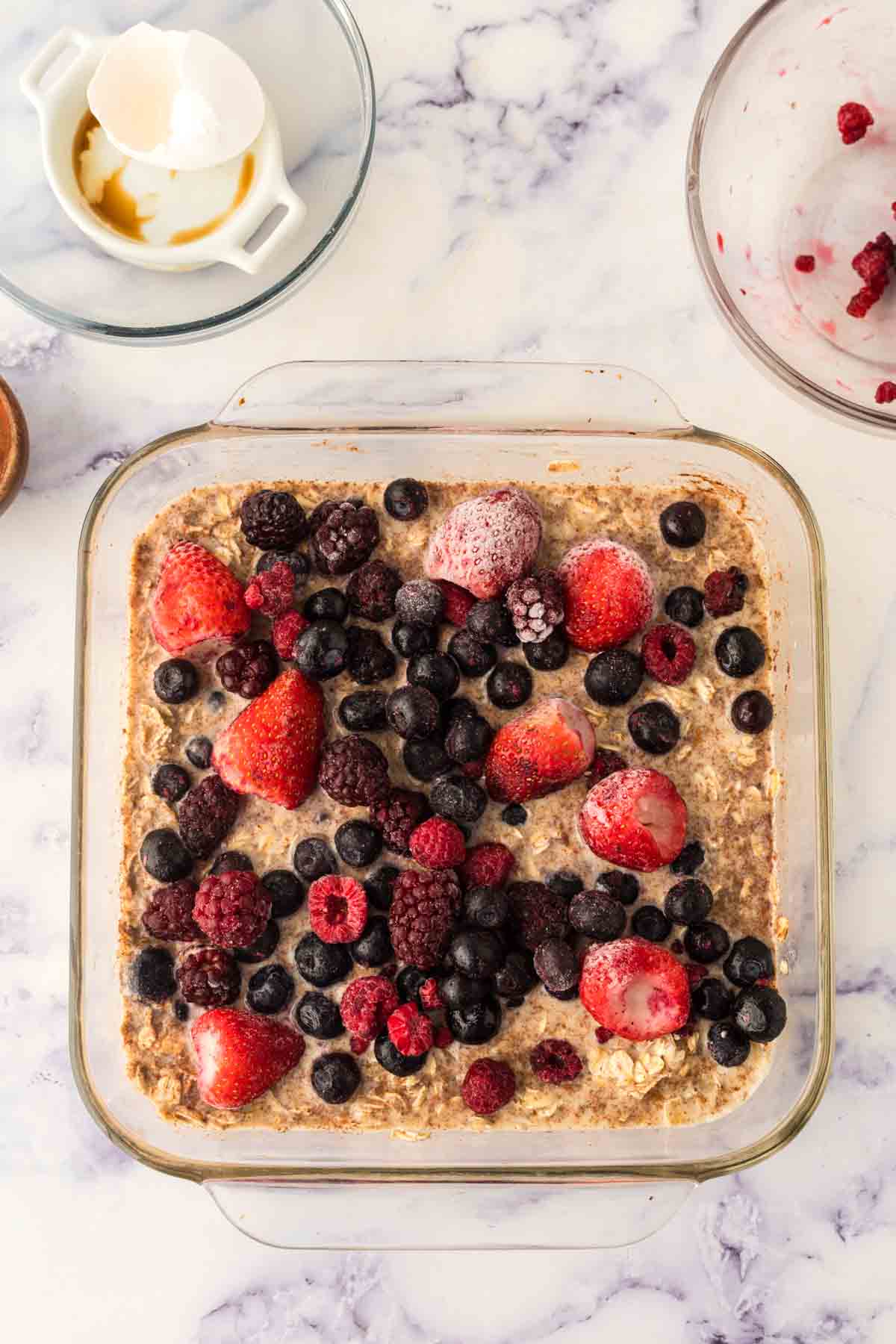 clear square casserole dish with baked oatmeal ingredients and fresh fruit inside