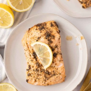 baked salmon filet on a round plate with a thin lemon slice on top.