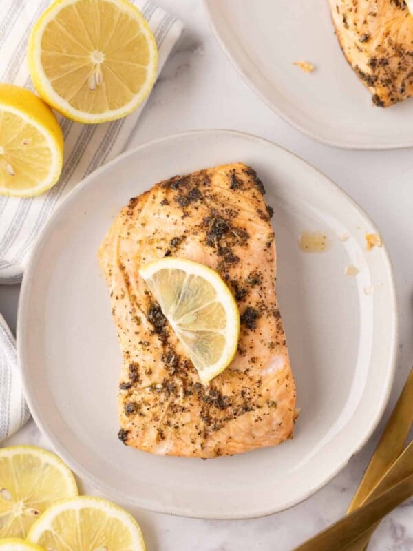 baked salmon filet on a round plate with a thin lemon slice on top.