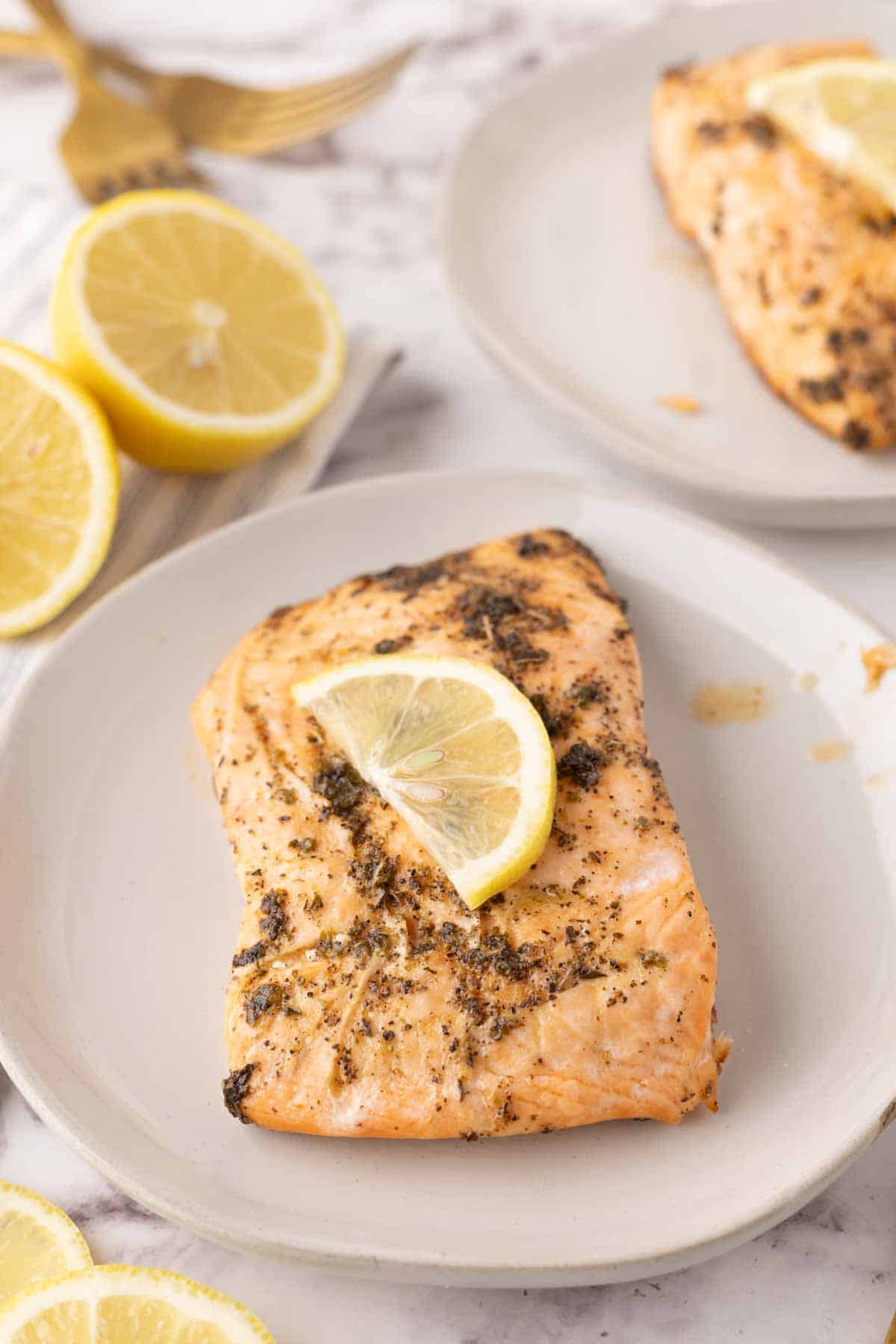 baked salmon filet dinner on a round white plate with a thing lemon slice