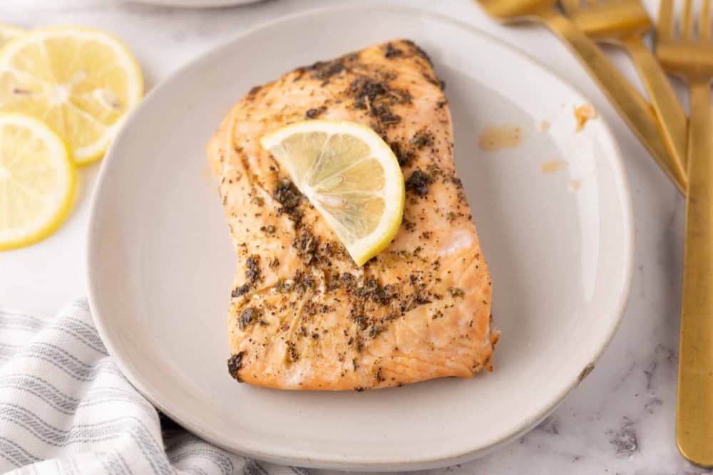 baked salmon filet on a round plate with a thin lemon slice on top.