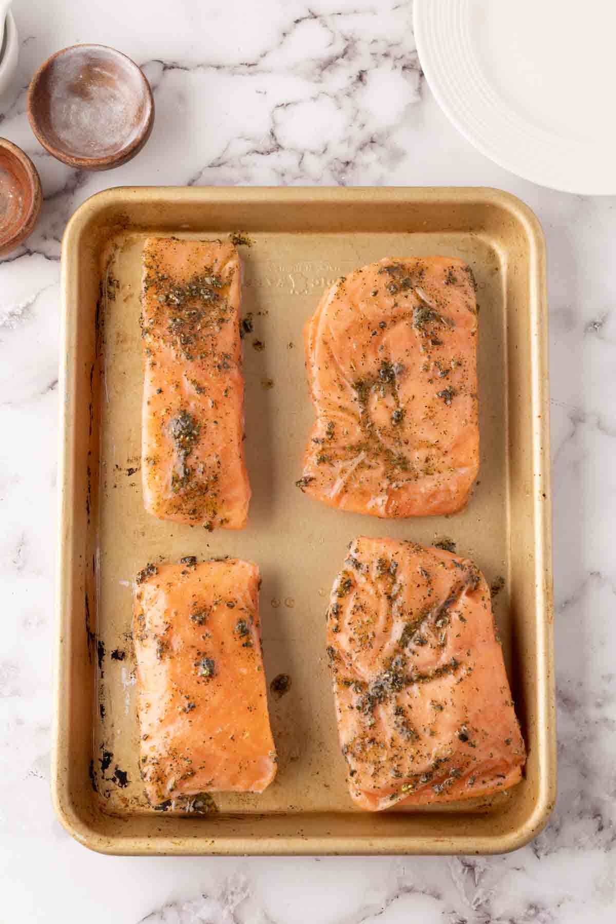 four salmon filets seasoned on a cookie tray before baking