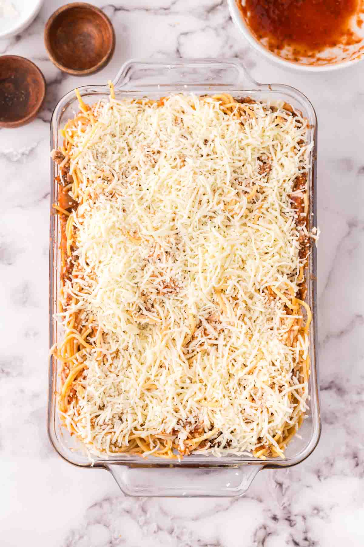 Assembling the baked spaghetti in a 9x13 with sprinkled cheese on top.