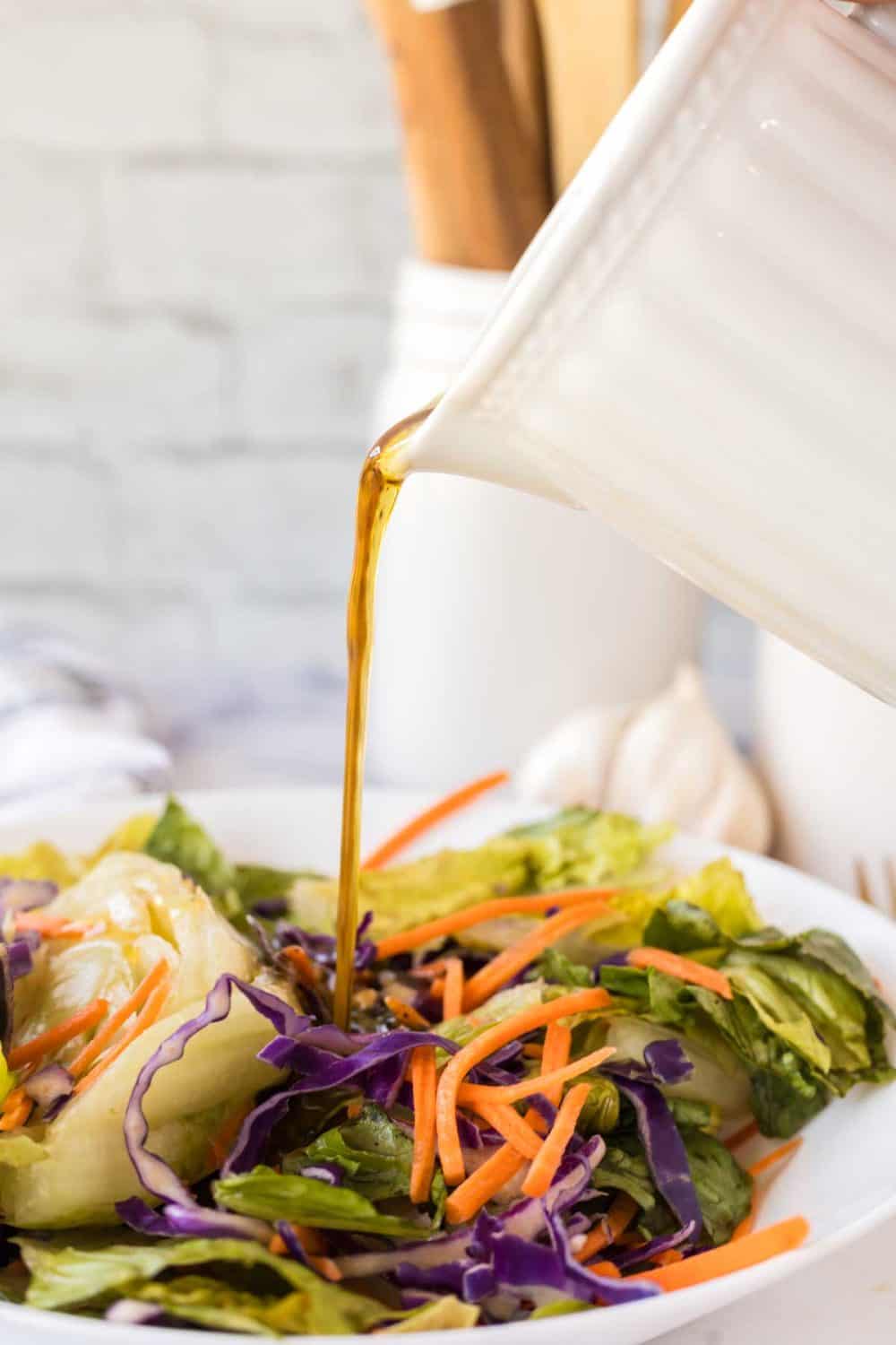 small white pitcher filled with balsamic vinaigrette pouring over a salad