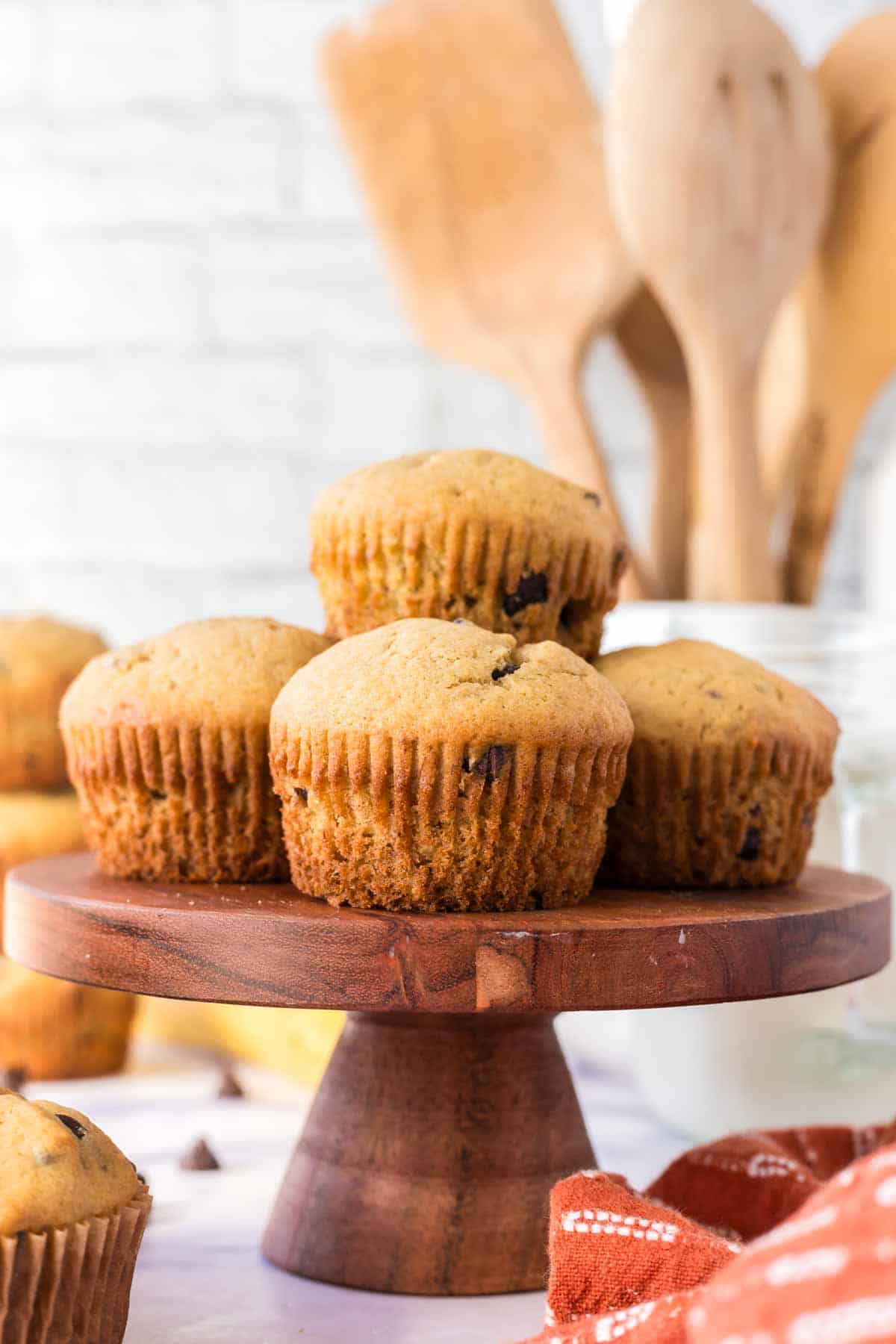 a wooden cake stand with banana chocolate chip muffins stacked on it
