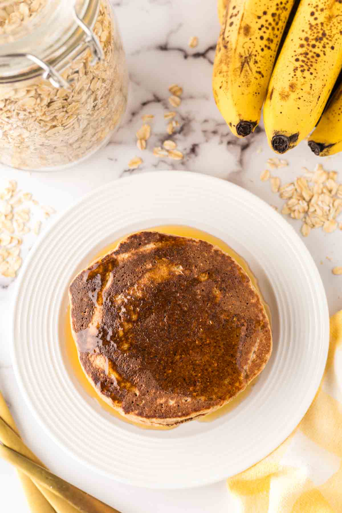 top aesthetic view of a stack of banana oatmeal pancakes on a white plate with syrup on top