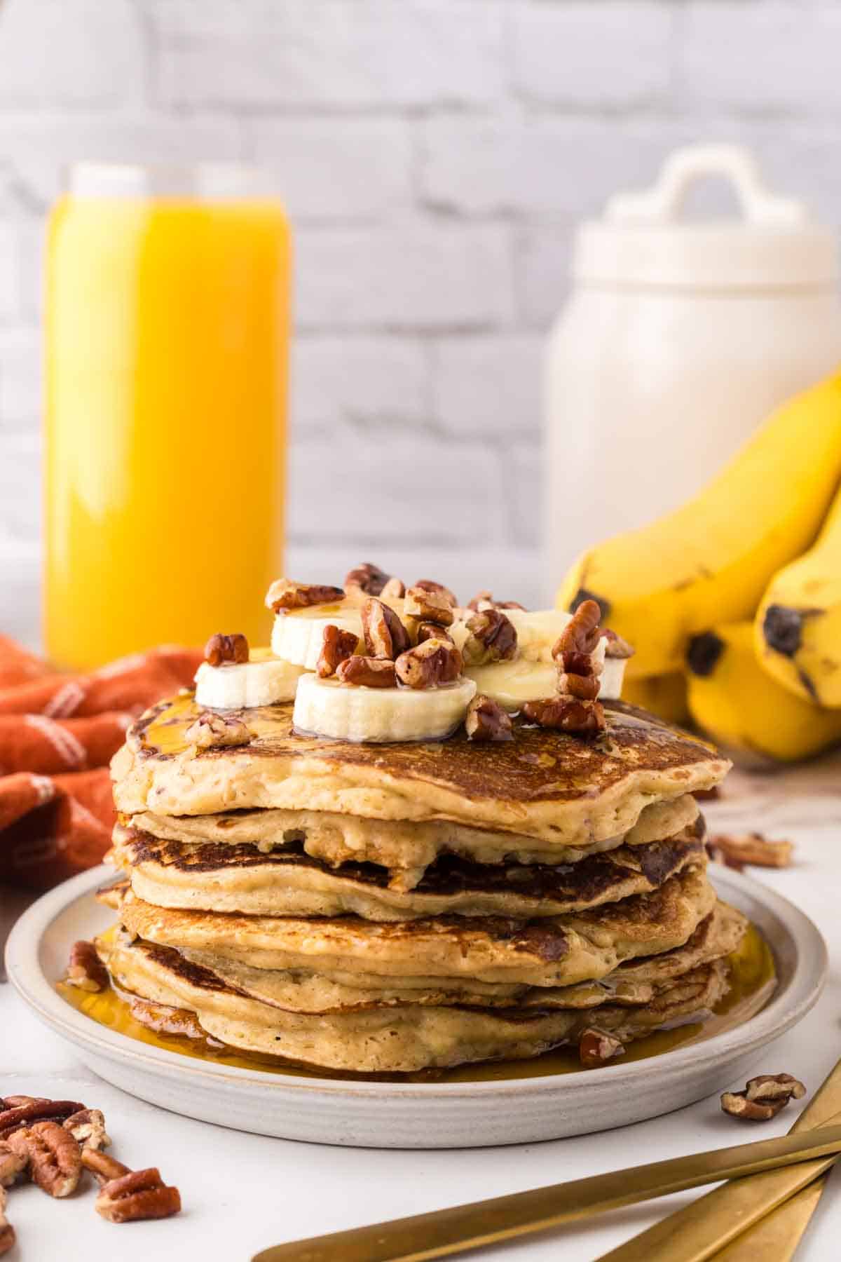 side view of a stack of banana pancakes on a round plate with walnuts and bananas with syrup on top