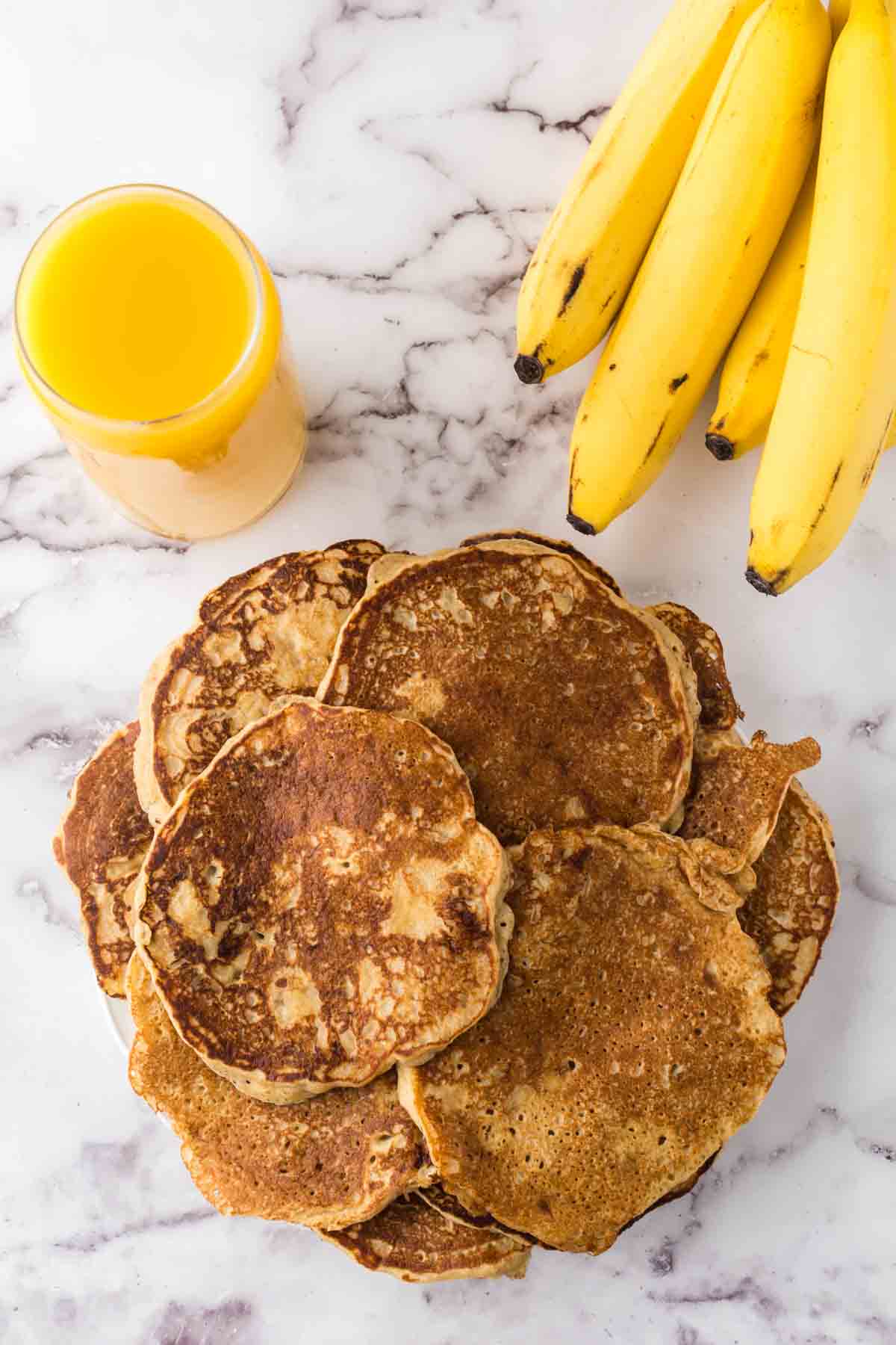 stack of banana pancakes with bananas and a top view of a glass of orange juice