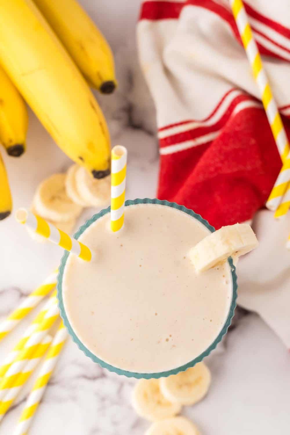 Top view of banana smoothie in a glass with bananas on the side.