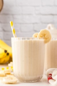Banana smoothie in a glass with a straw and bananas.