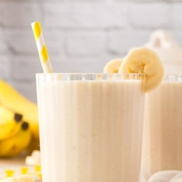Banana smoothie in a glass with a straw and bananas.