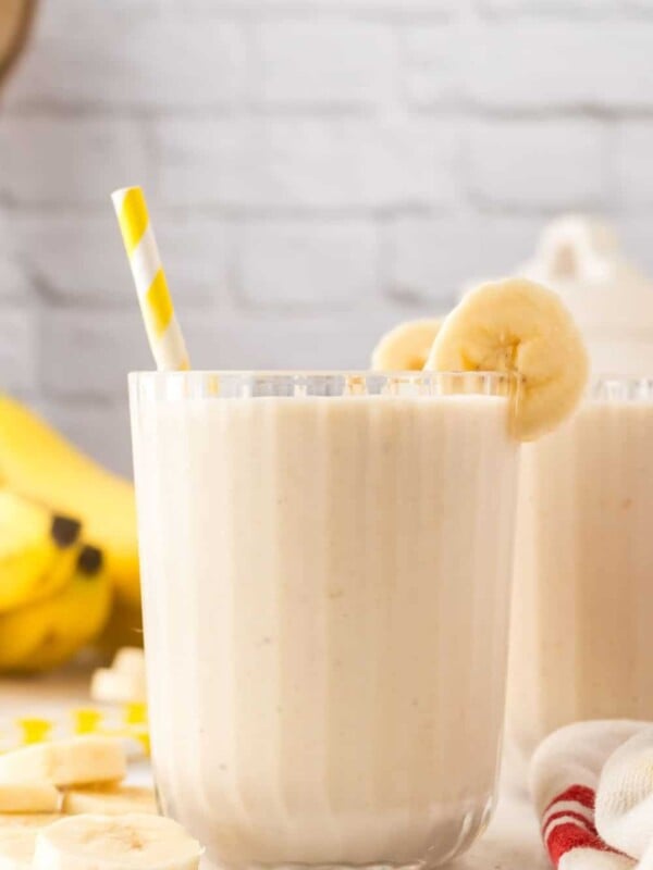 Banana smoothie in a glass with a straw and bananas.