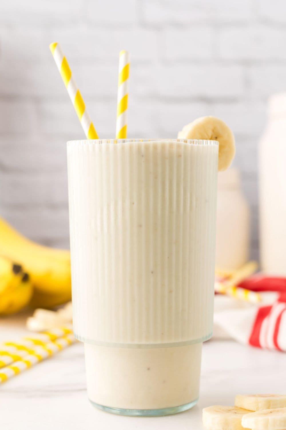 Banana smoothie in a glass with 2 straws.