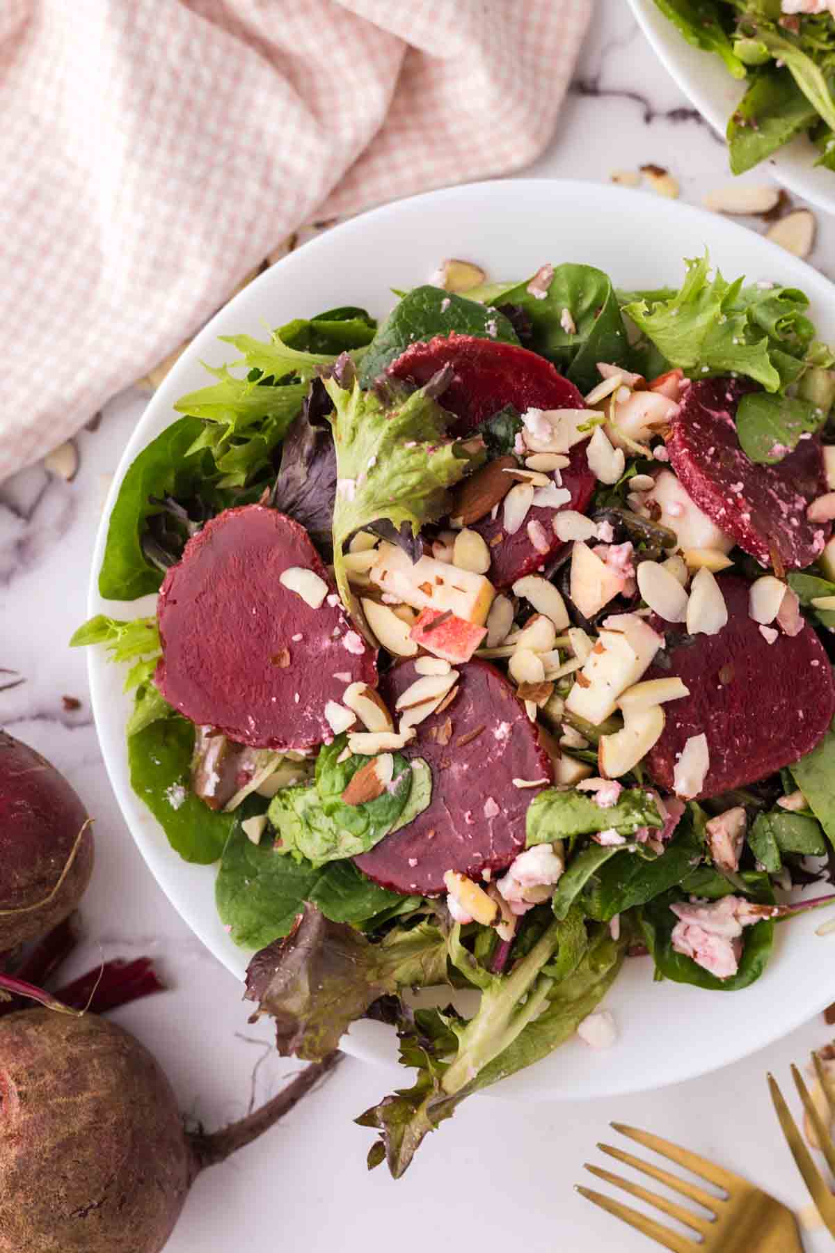 White bowls of beet salad with golden forks to the side.