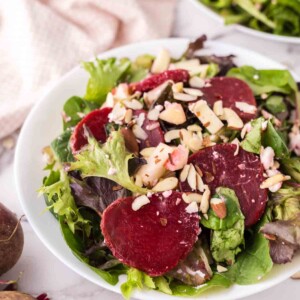 Two white bowls of beet salad with golden forks inside.