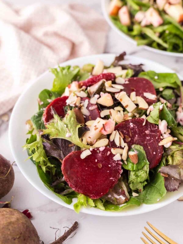 Two white bowls of beet salad with golden forks inside.