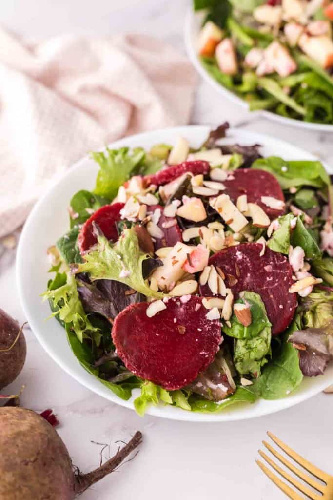 Two white bowls of beet salad with golden forks inside.